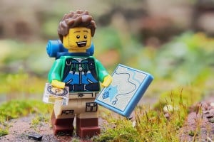 Lego mini figure holding a map and compass, hiking in the woods